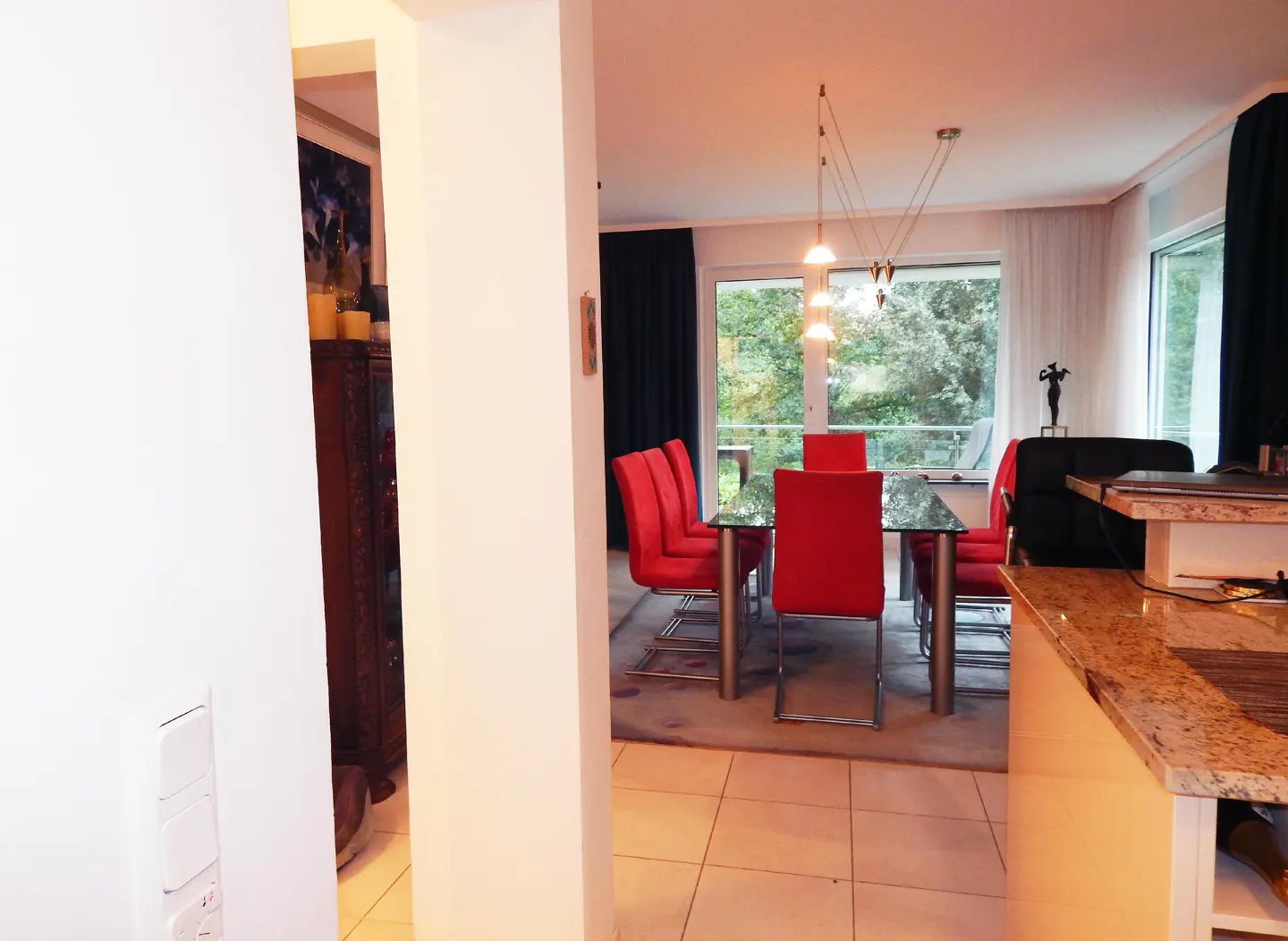 A bright dining room with red chairs and a glass table, viewed through a doorway.