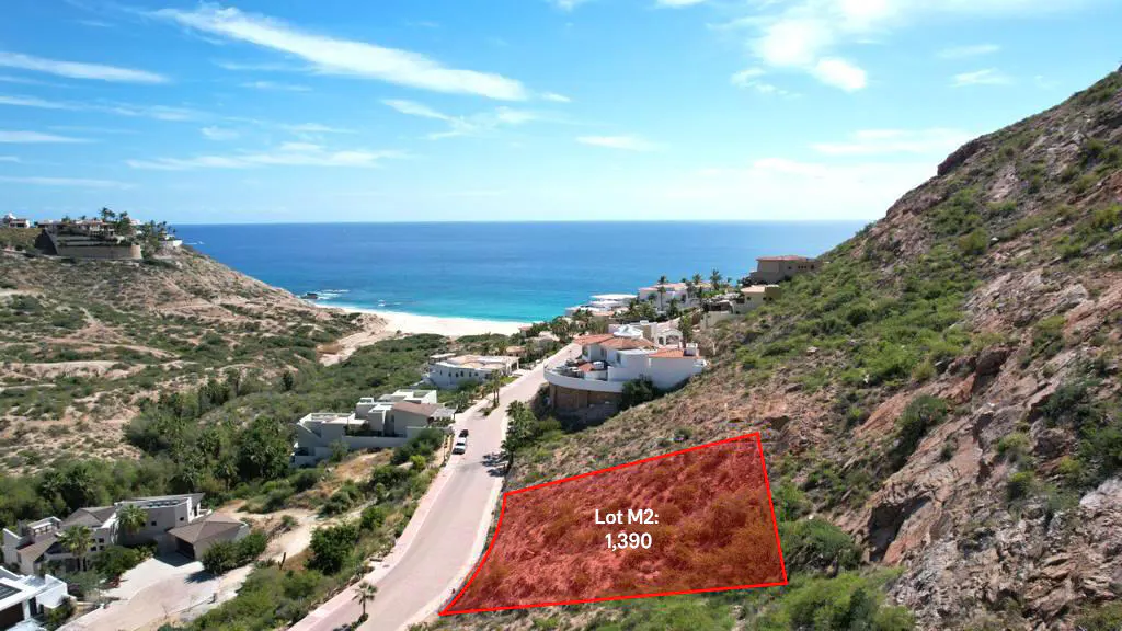 View of Lot M2, 1,390, outlined in red, on a hillside near the ocean. Houses and a road are visible. The sky is blue.