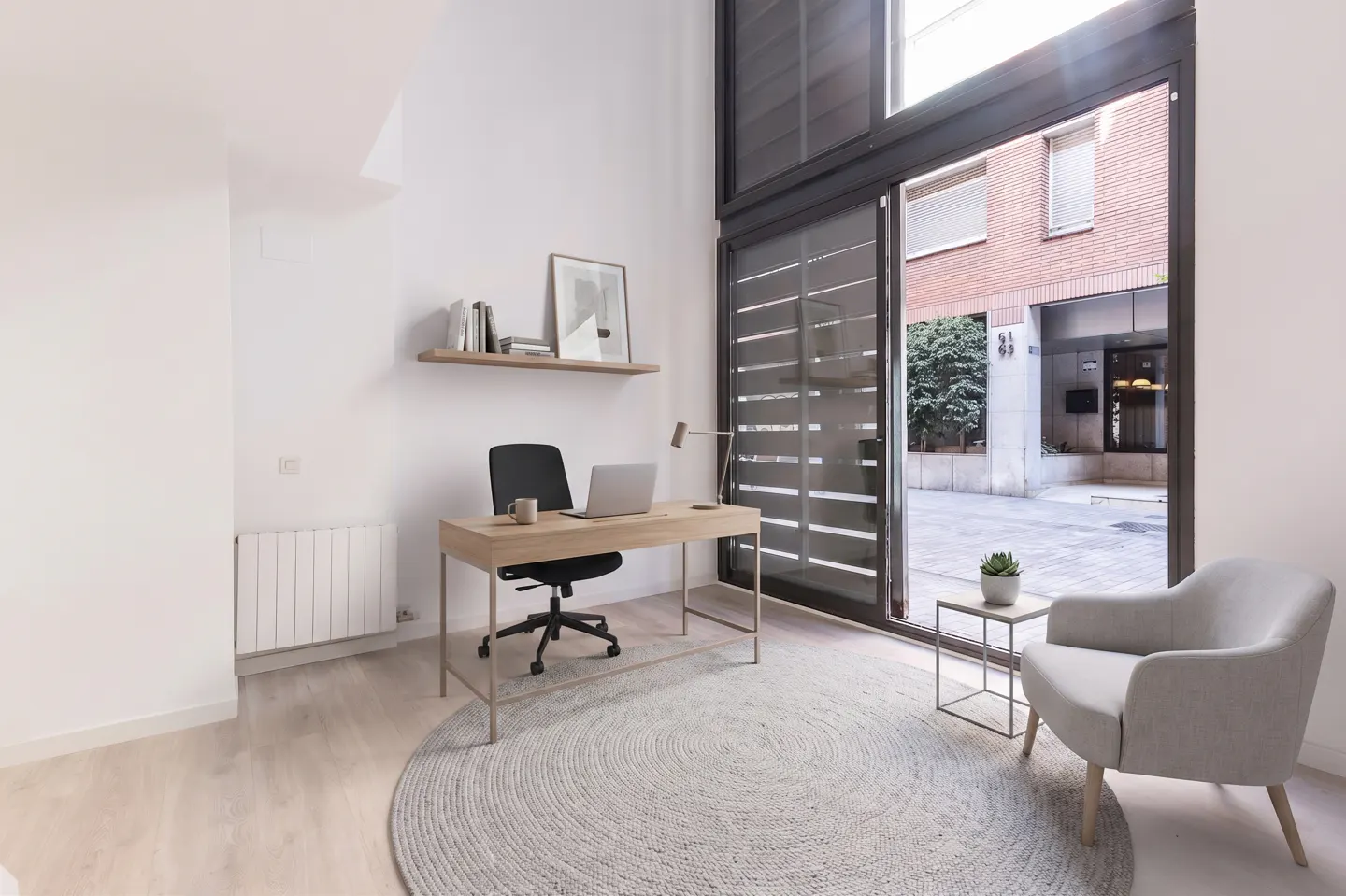 Bright home office with desk, laptop, chair, and open sliding doors to a courtyard. A round rug sits under the desk and chair.