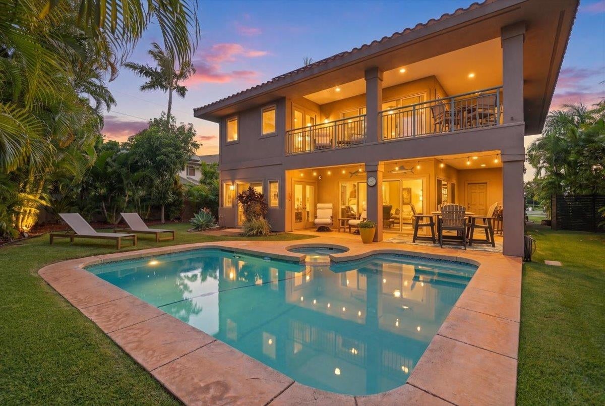 Two-story house with a pool, patio, and balcony at sunset, featuring lounge chairs and lush tropical landscaping. [AI-generated text]