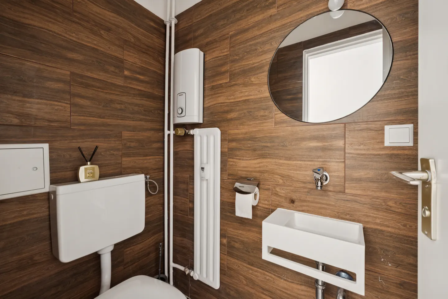Bathroom with wood-look tile, white toilet, sink, radiator, and oval mirror.