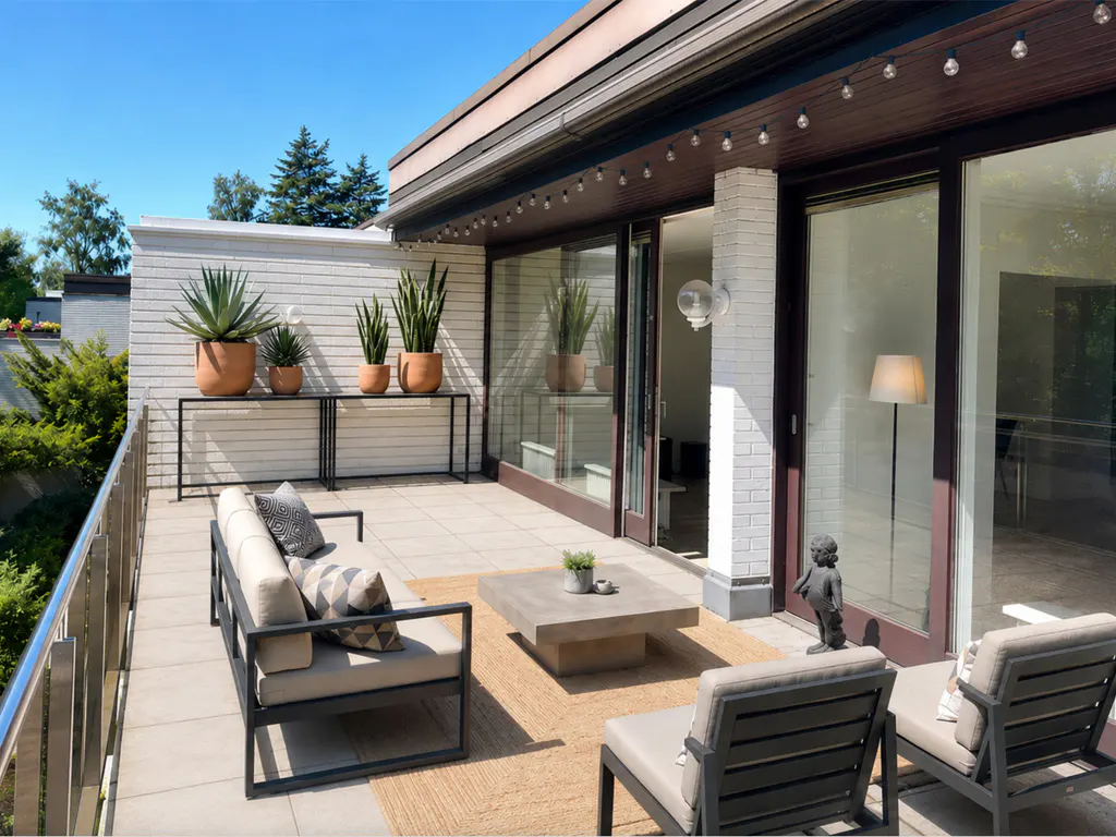 Outdoor patio with a sofa, chairs, and a table with plants. Sliding glass doors lead inside. String lights hang above.