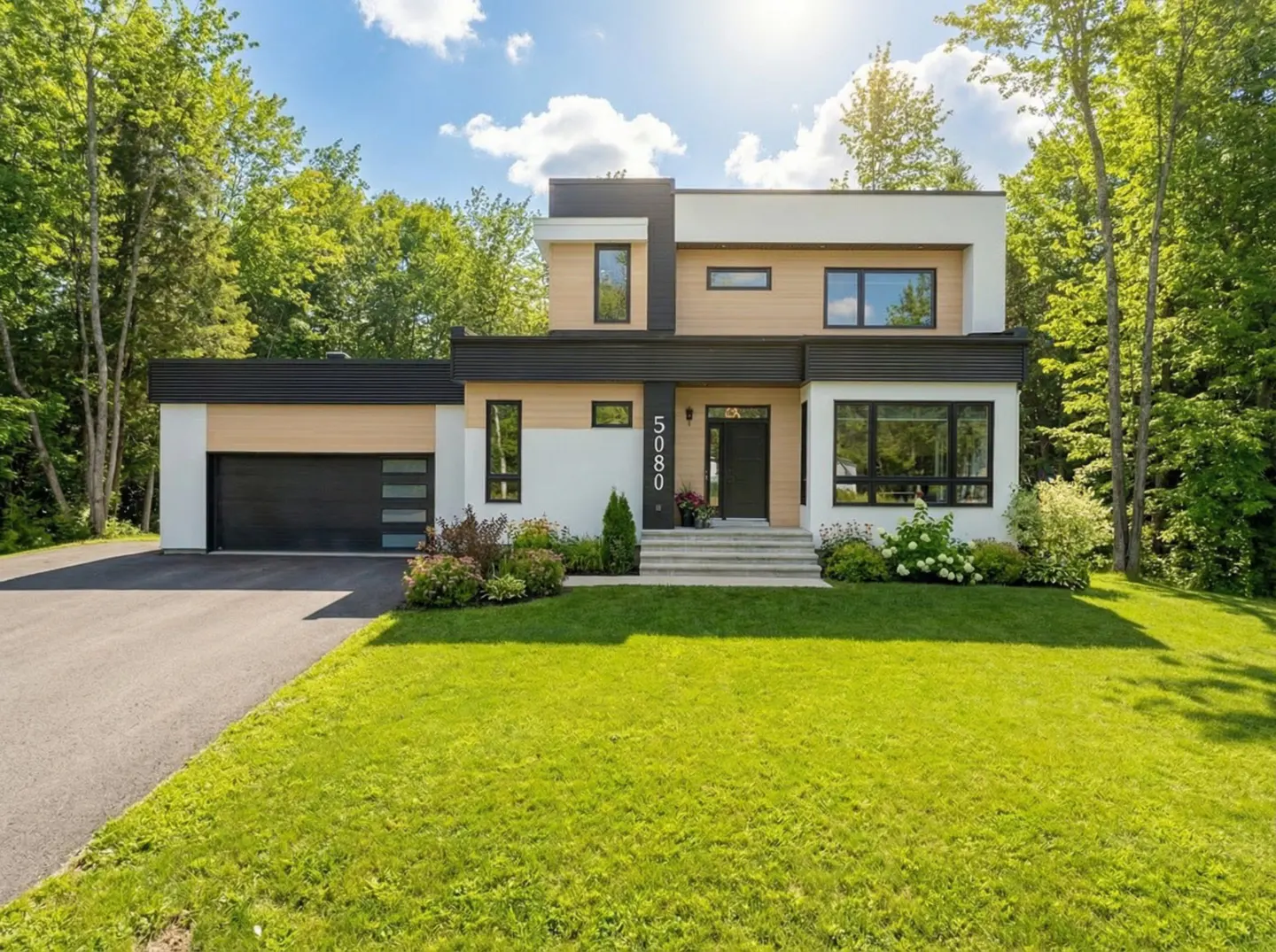Two-story modern home with a black garage door, white siding, and a green lawn. The house number 5080 is visible above the front door.