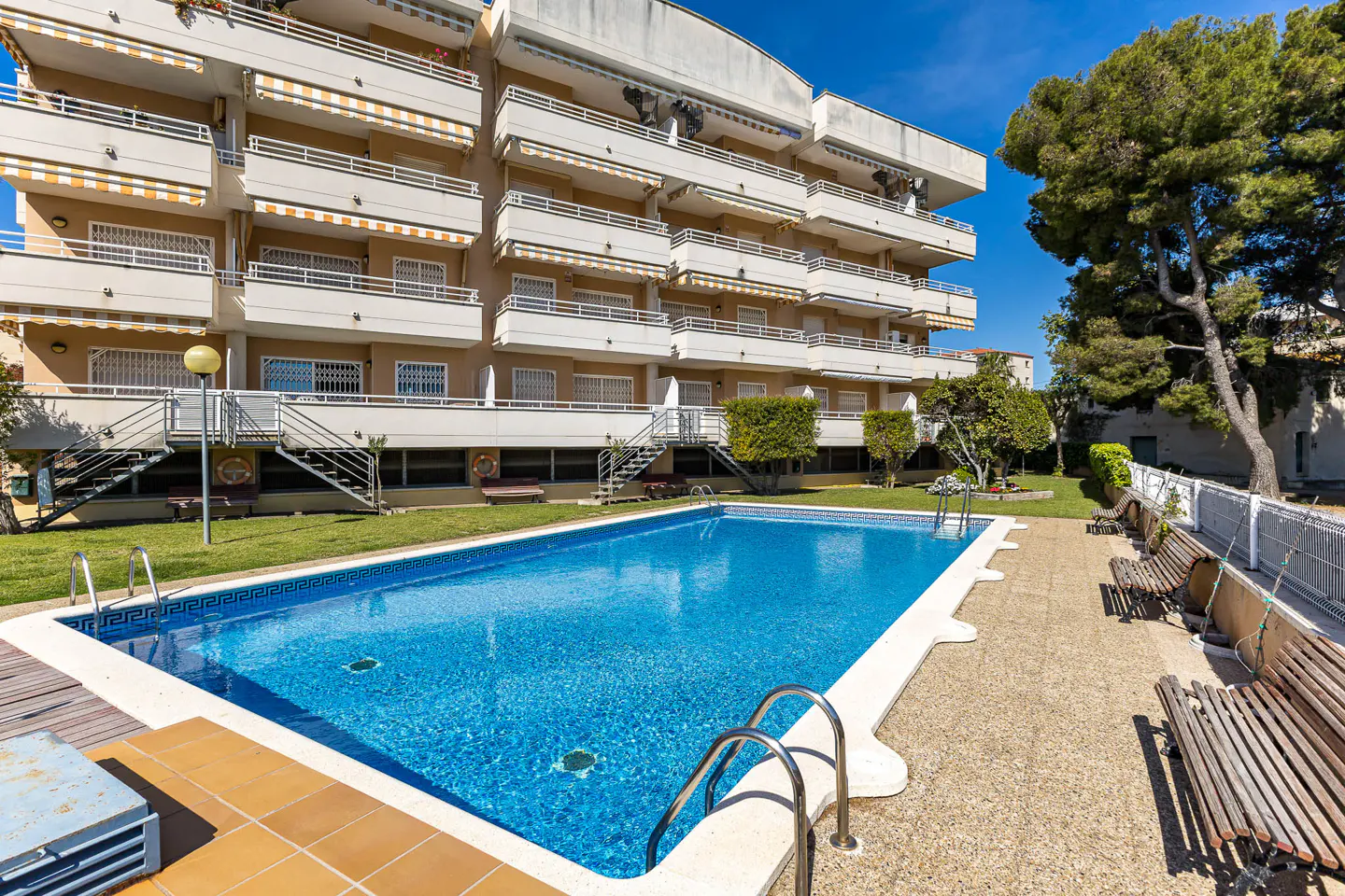 Exterior view of a multi-story apartment building with a blue swimming pool in the foreground.