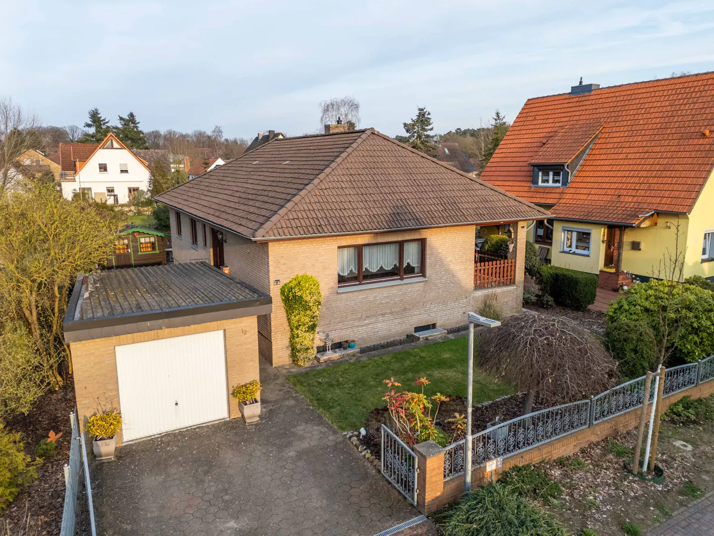 Aerial view of a tan brick house with a brown tiled roof, a white garage door, and a small front yard.