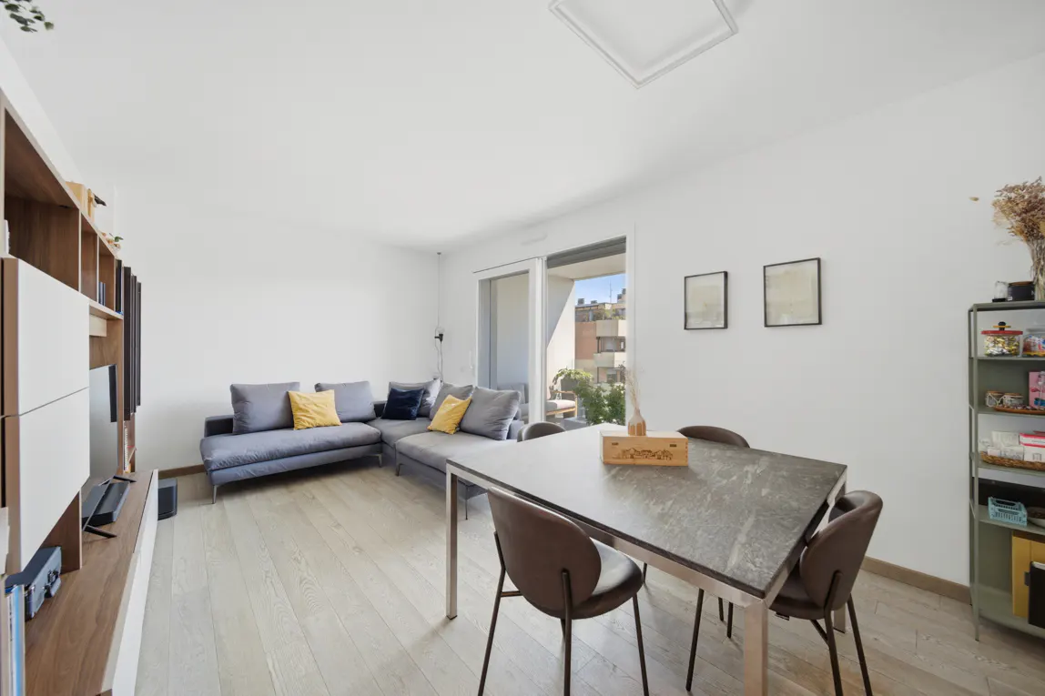 Bright living room with gray sectional sofa, yellow pillows, and a gray dining table with brown chairs. Shelving unit on the left.