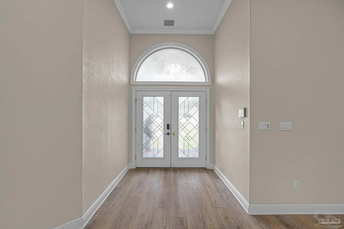 Entryway with light beige walls, wood-look flooring, and white double doors featuring a decorative arched glass window.