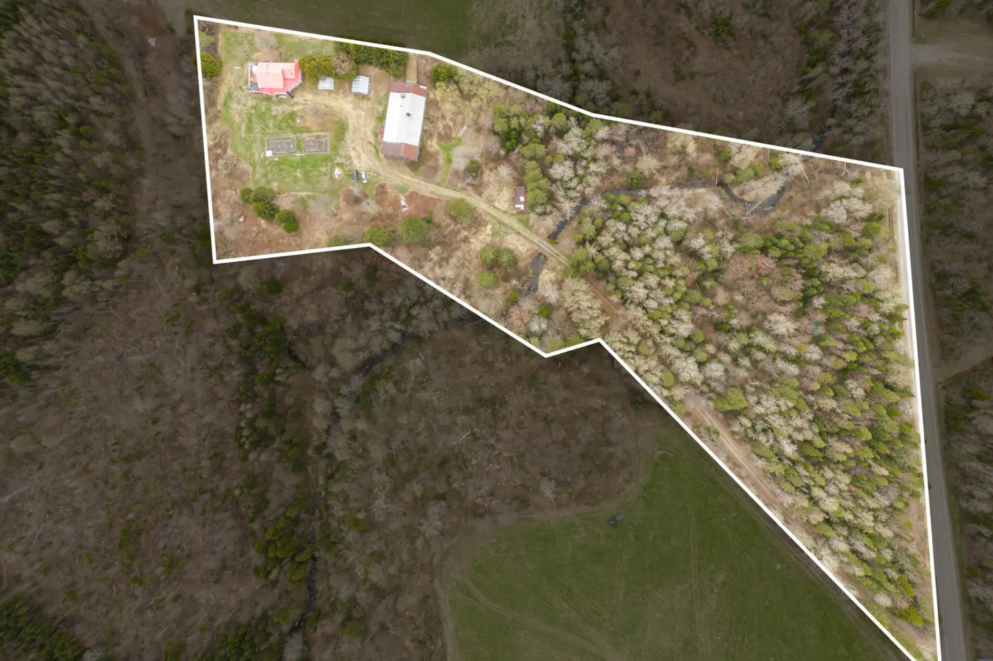 Aerial view of a property outlined in white, featuring a red-roofed house, barn, stream, and mixed forest.
