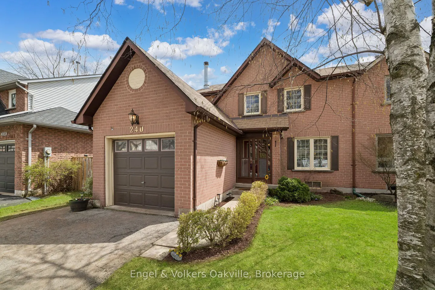 Two-story brick house with brown shutters, garage, and green lawn under a blue sky.