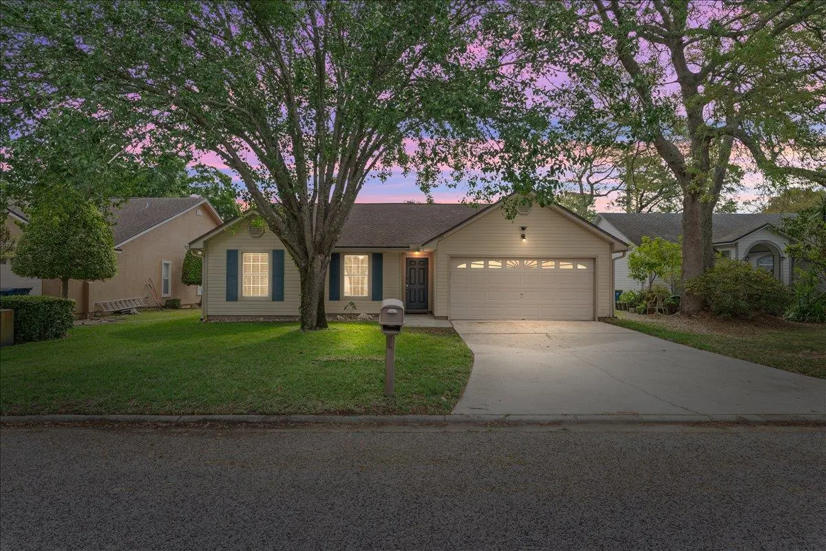 Beige single-story house with blue shutters and a two-car garage at dusk. Large trees frame the house.