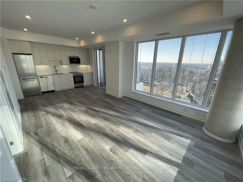 Bright, modern condo interior with gray wood floors, white cabinets, stainless steel appliances, and large windows with a city view.