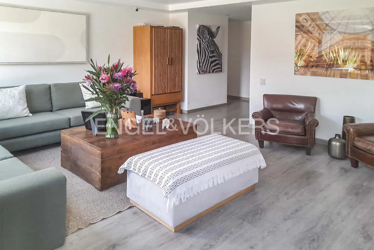 Modern living room with a sage green sofa, wooden coffee table, white ottoman, and two brown leather armchairs.