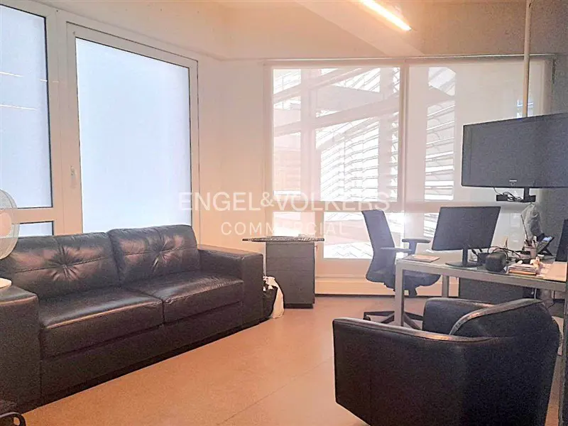 Office space with a black leather sofa and chair, desk, and large windows with blinds. Engel & Volkers logo in the background.