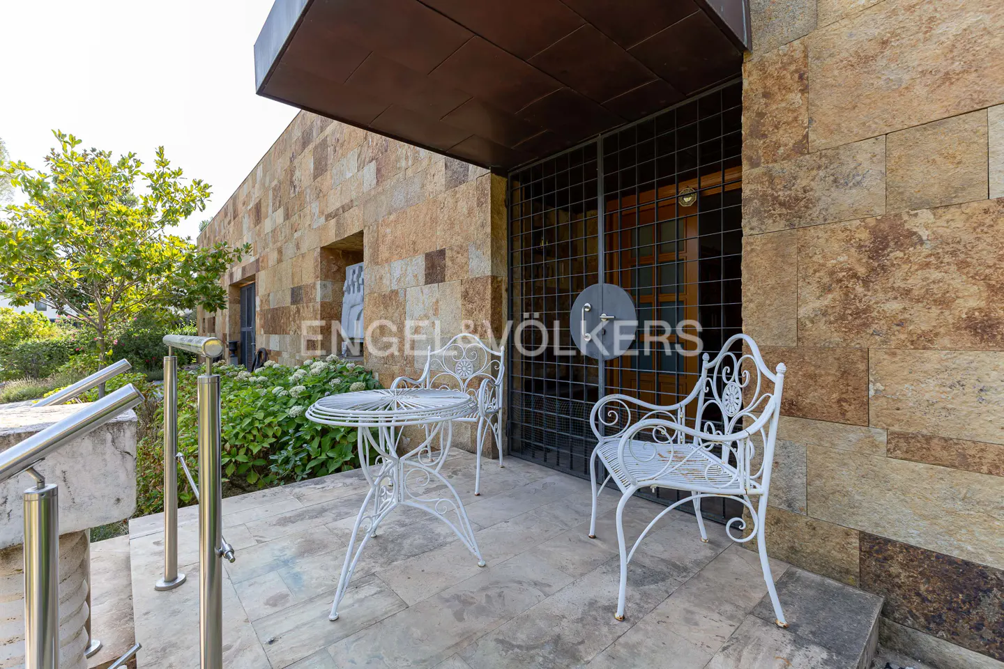 White wrought iron table and chairs on a stone patio in front of a modern house with a metal security gate.