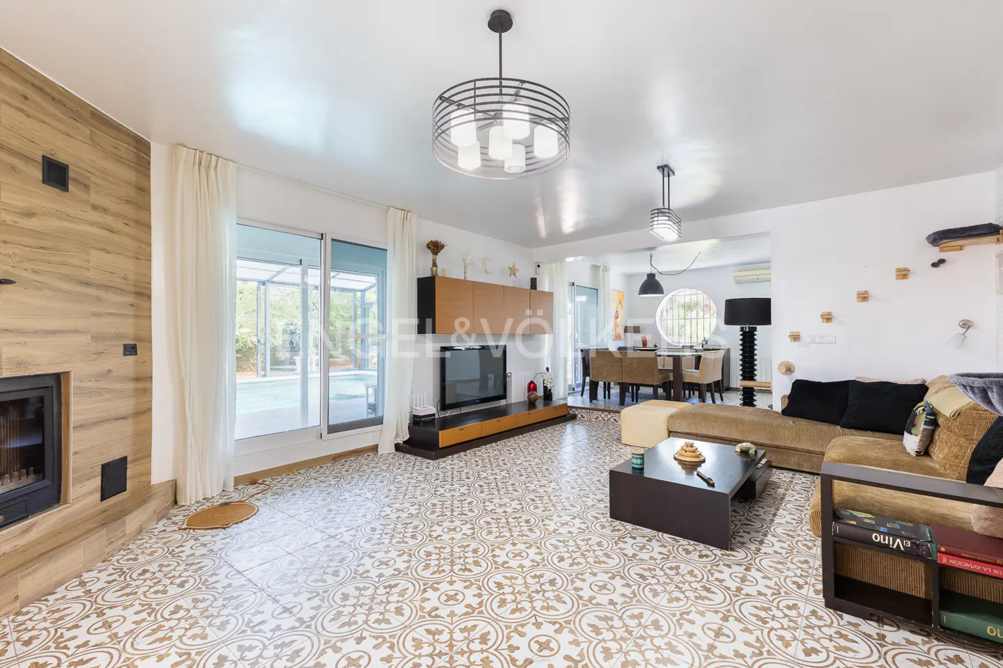 Bright living room with patterned tile floor, fireplace, tan sofa, and dining area in the background.