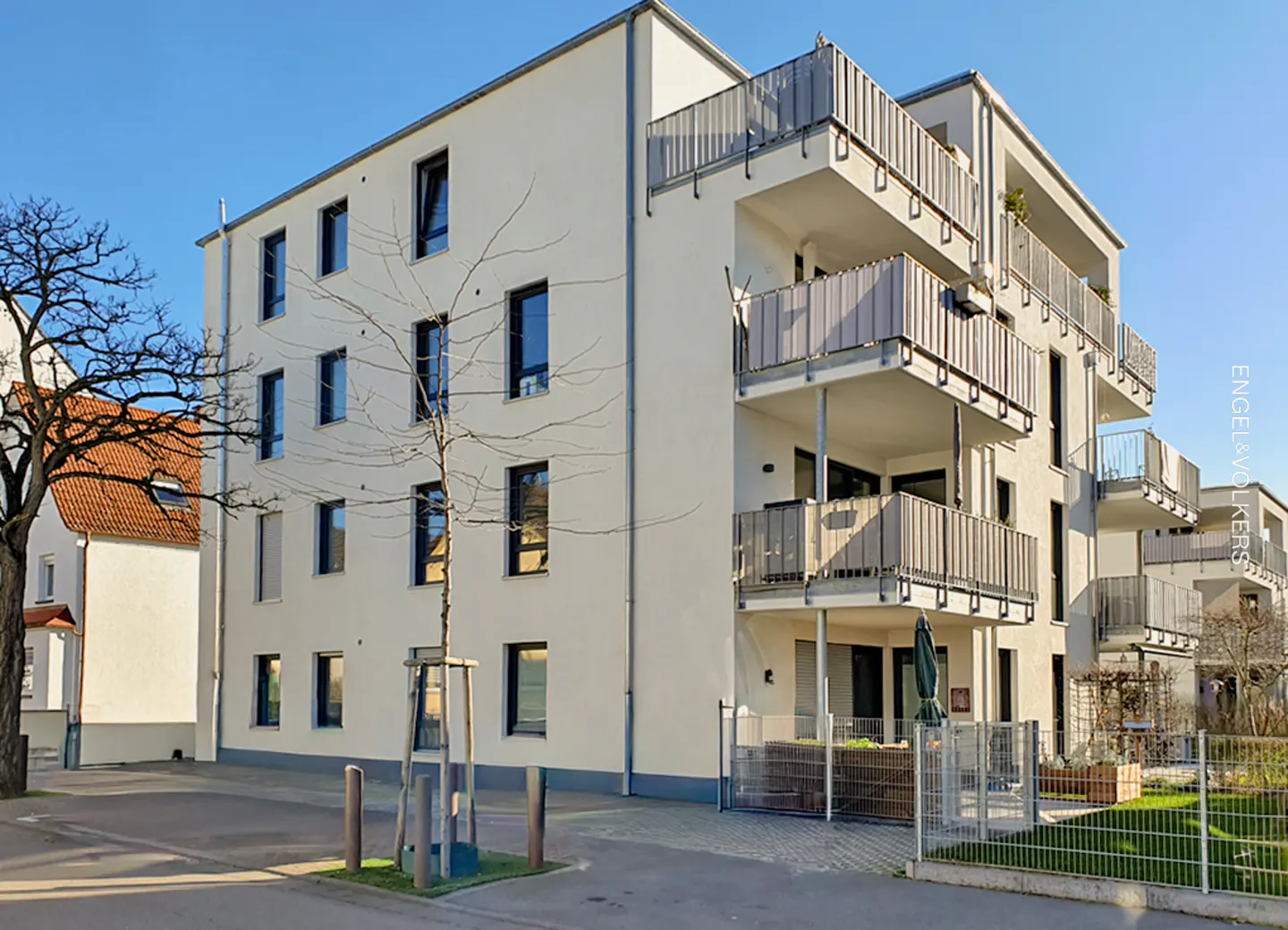Exterior view of a modern, multi-story apartment building with balconies and a light beige facade under a clear blue sky.