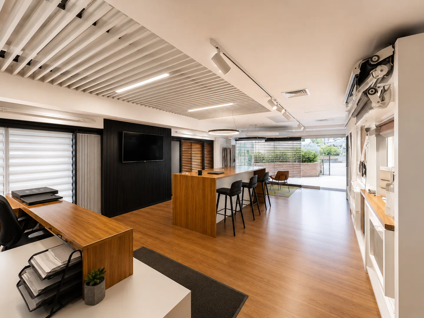 Modern office with wood floors, a central kitchen island with bar stools, a black accent wall with TV, and white ceiling.