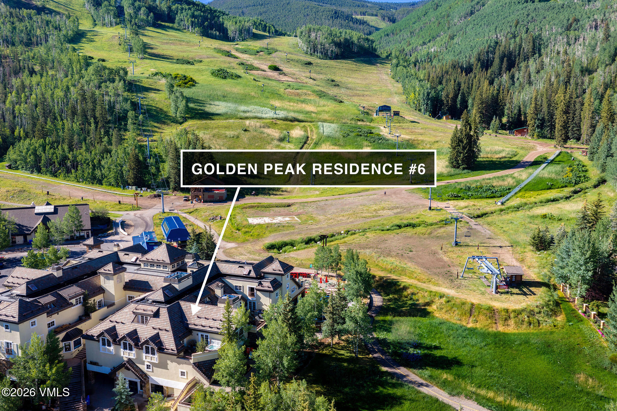 Aerial view of a luxury residence at the base of a lush green mountain ski slope with chairlifts and forest scenery.