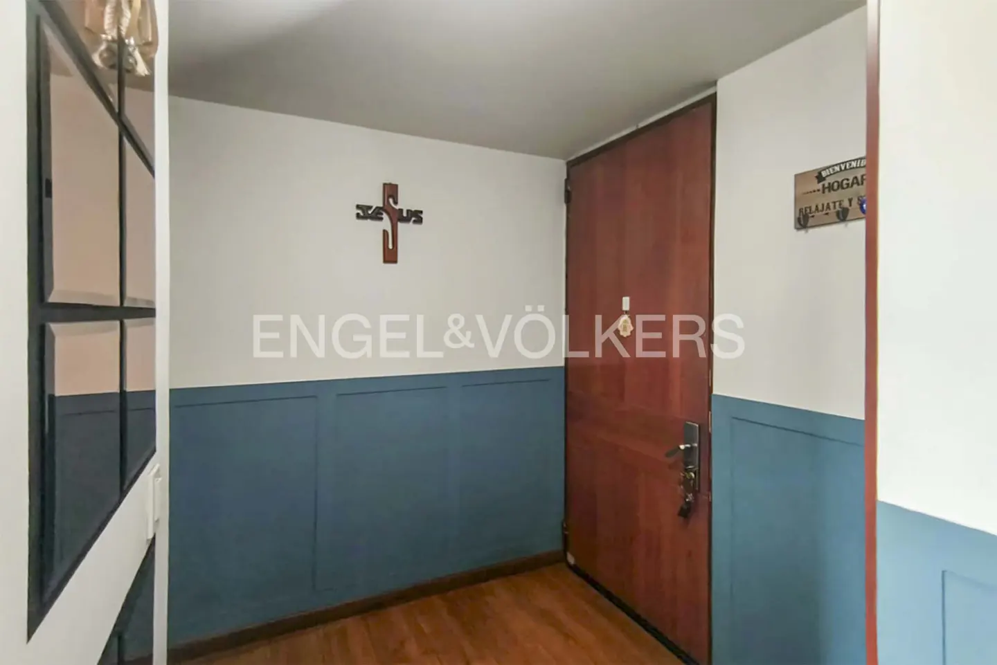 Entryway with a wooden door, blue wainscoting, and a wooden cross on the wall. The Engel & Völkers logo is visible.