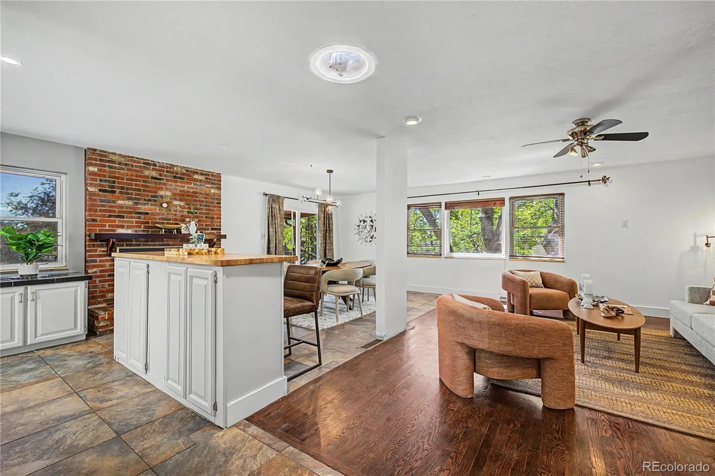 Open-concept living space with a kitchen island, dining area, and living room. Two brown chairs face a coffee table on a striped rug.