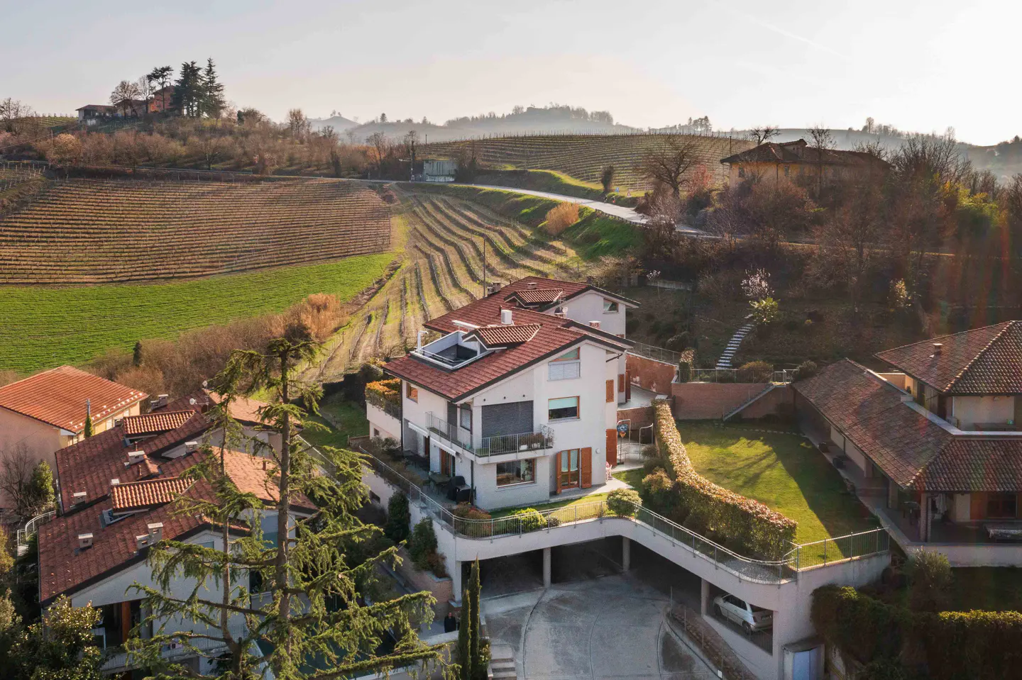 Aerial view of a modern white house with a red tile roof, surrounded by lush greenery and vineyards on a sunny day.