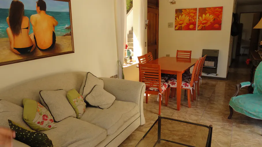 Living room with a beige sofa, wooden dining table with chairs, and a painting of a couple by the sea.