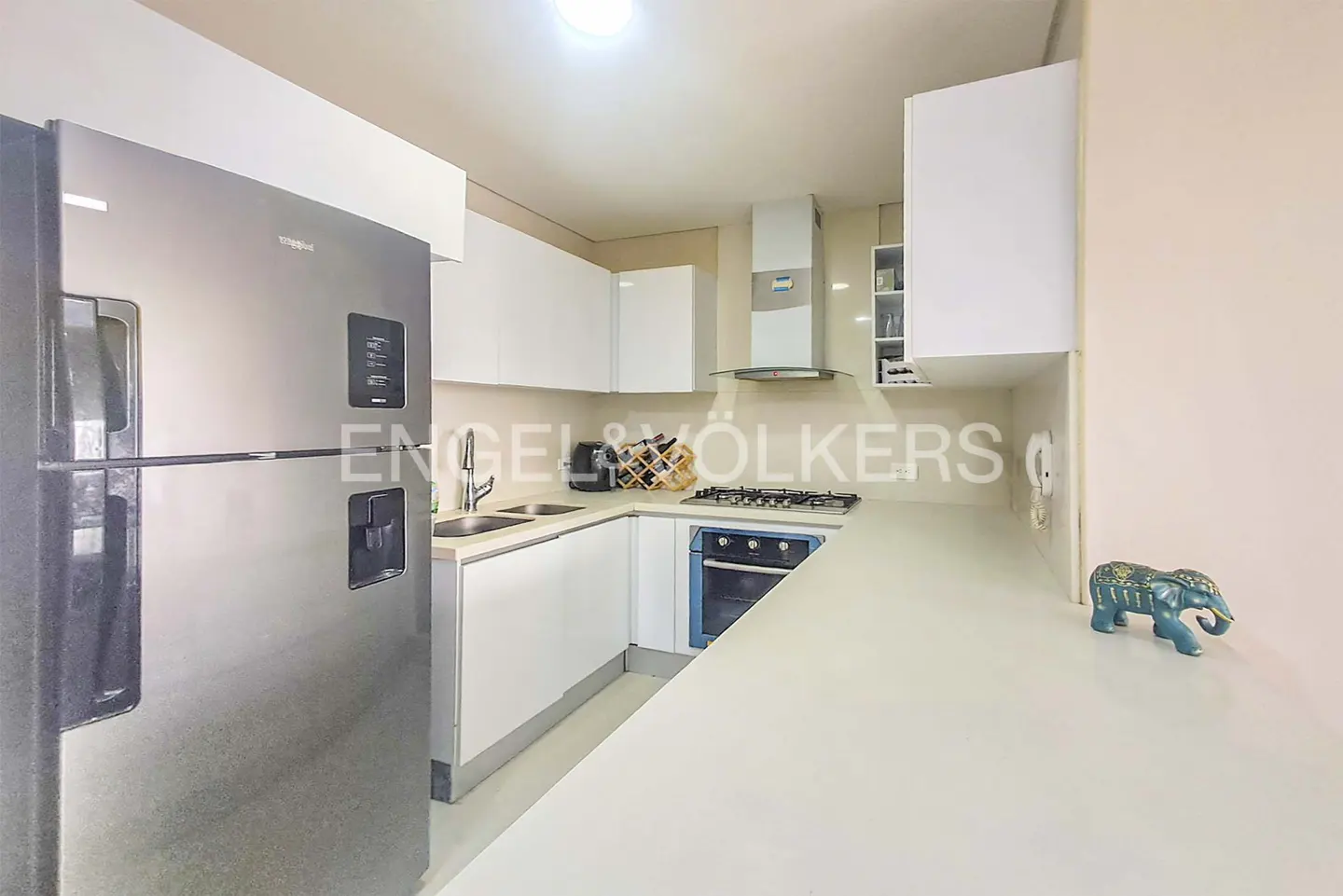 A modern kitchen with white cabinets, stainless steel appliances, and a blue elephant figurine on the counter.