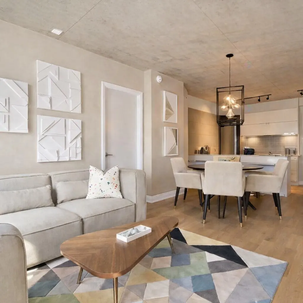 A modern living room with a beige sofa, wood coffee table, geometric rug, and dining area with a black chandelier.