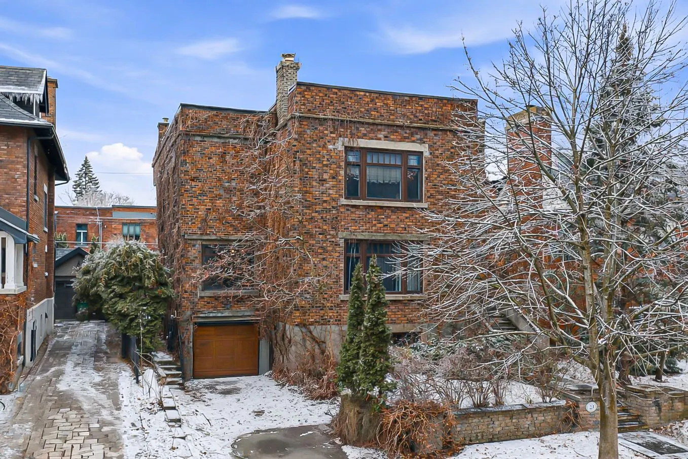 A two-story brick house with a brown garage door and vines on the walls in winter.