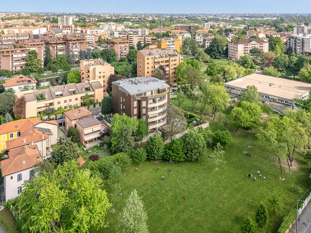 Aerial view of a city neighborhood with brown brick buildings, green trees, and a grassy park with people.