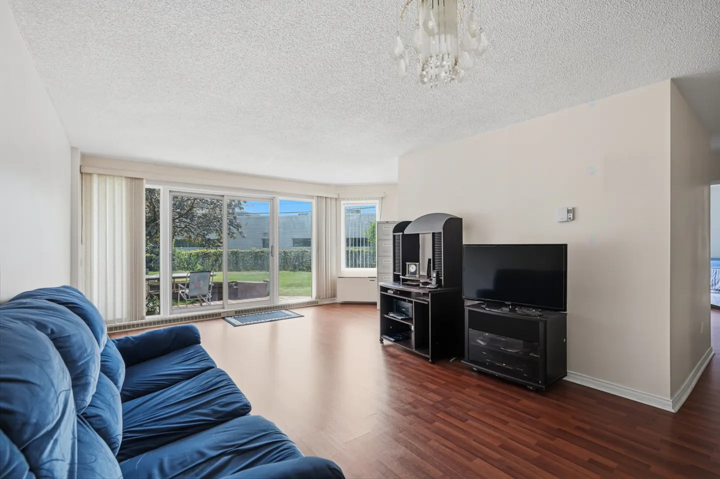 Living room with a blue sofa, dark wood floors, and sliding glass doors to a patio. A black TV stand and media center are against the wall.