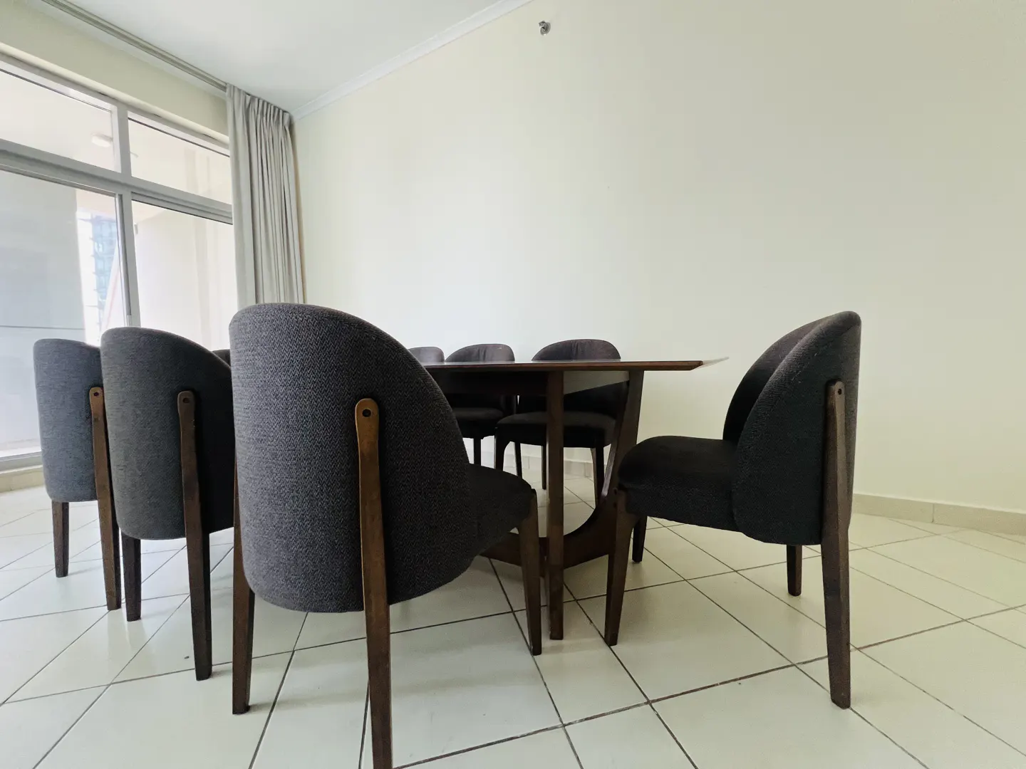 A dining room features a dark wood table surrounded by eight gray upholstered chairs with wooden legs.