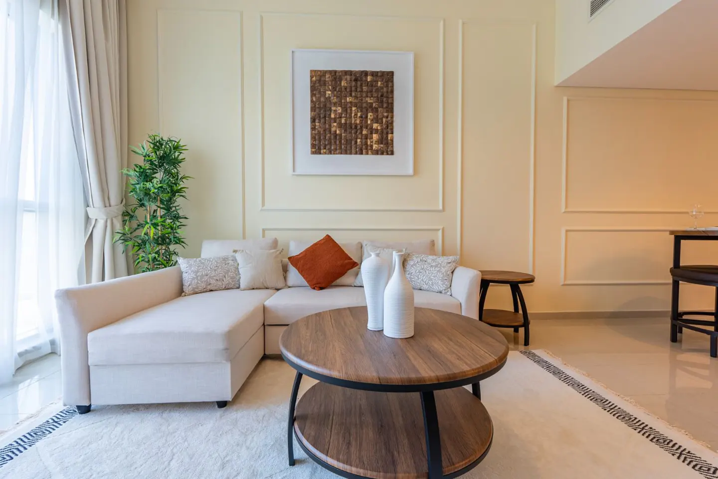 Living room with a cream-colored sectional sofa, round wood coffee table, and neutral walls with framed art.
