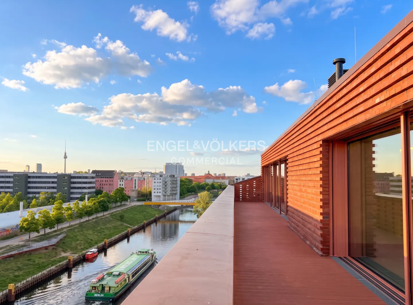 View from a red-brick building overlooking a canal in Berlin, Germany. A barge travels on the water, with the TV tower visible in the distance.