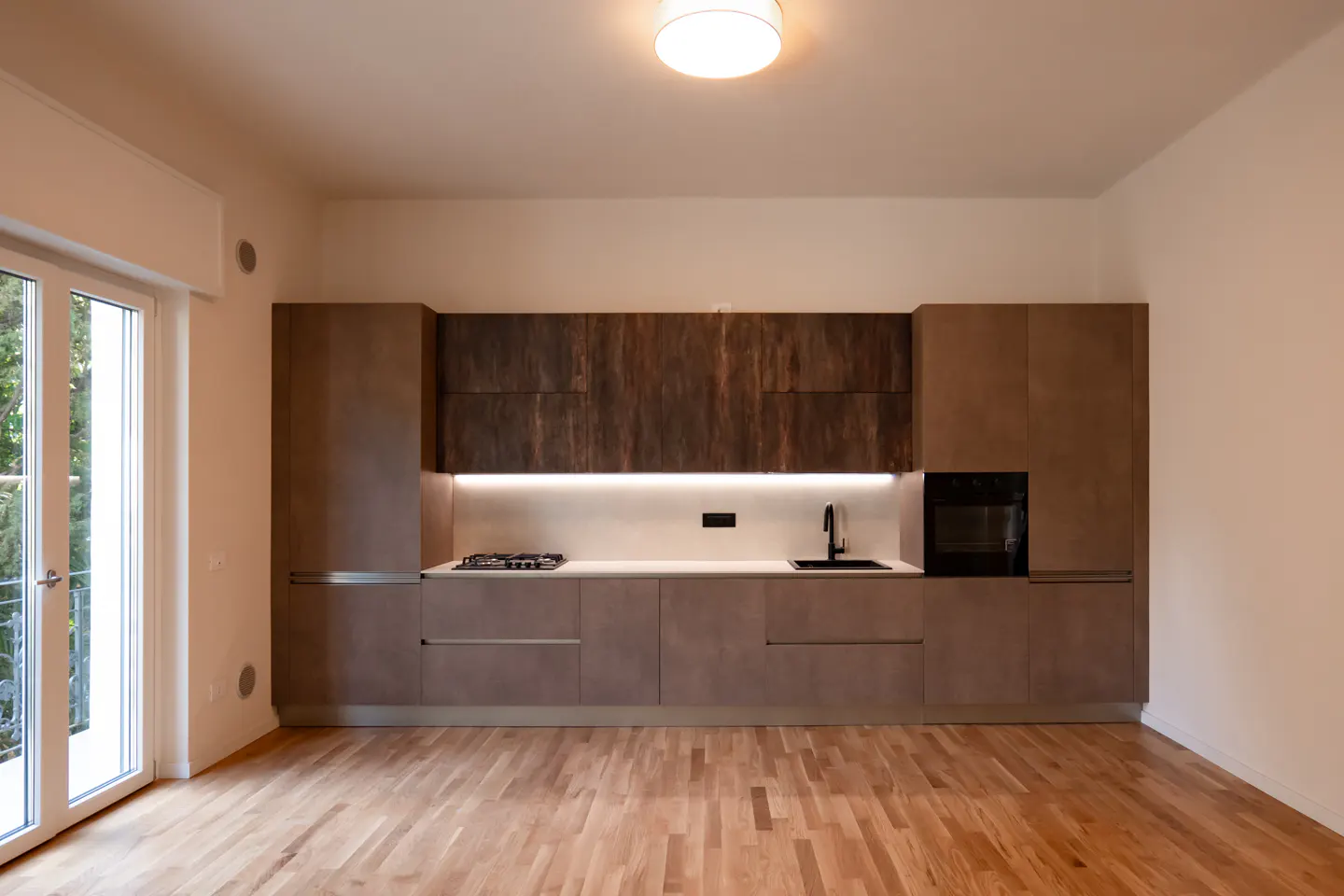 Modern kitchen with brown cabinets, white countertops, built-in oven, gas stove, and light wood floors near a glass door.