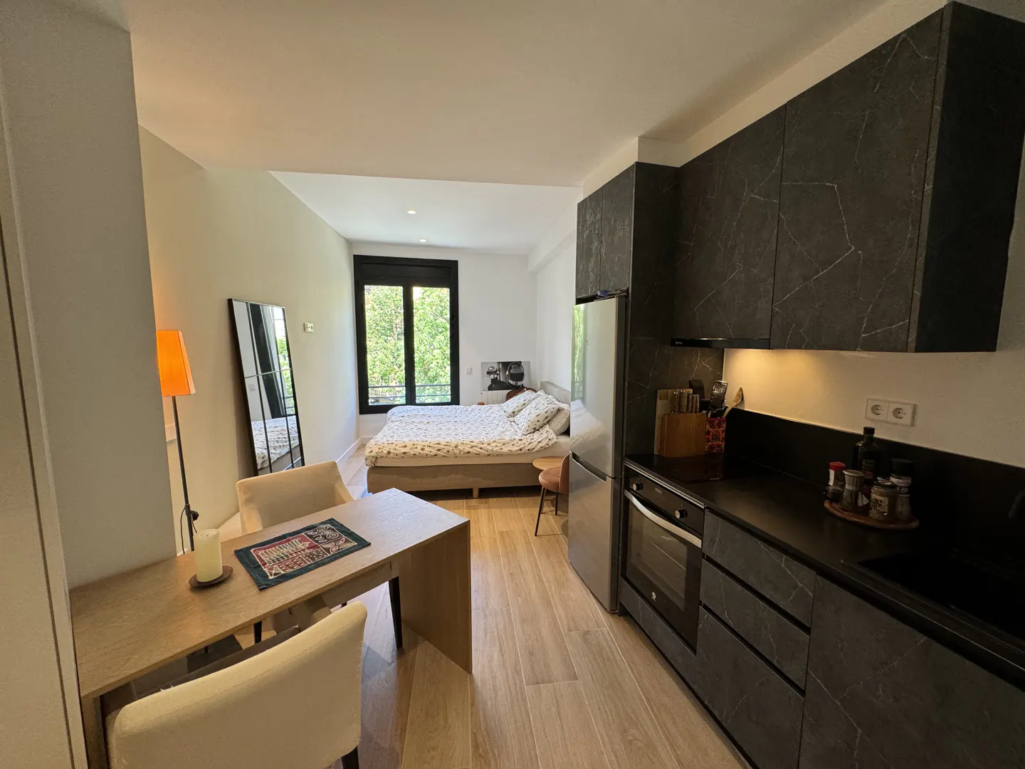 Studio apartment with a bed, dining table, and kitchen. The kitchen has dark gray cabinets and stainless steel appliances.