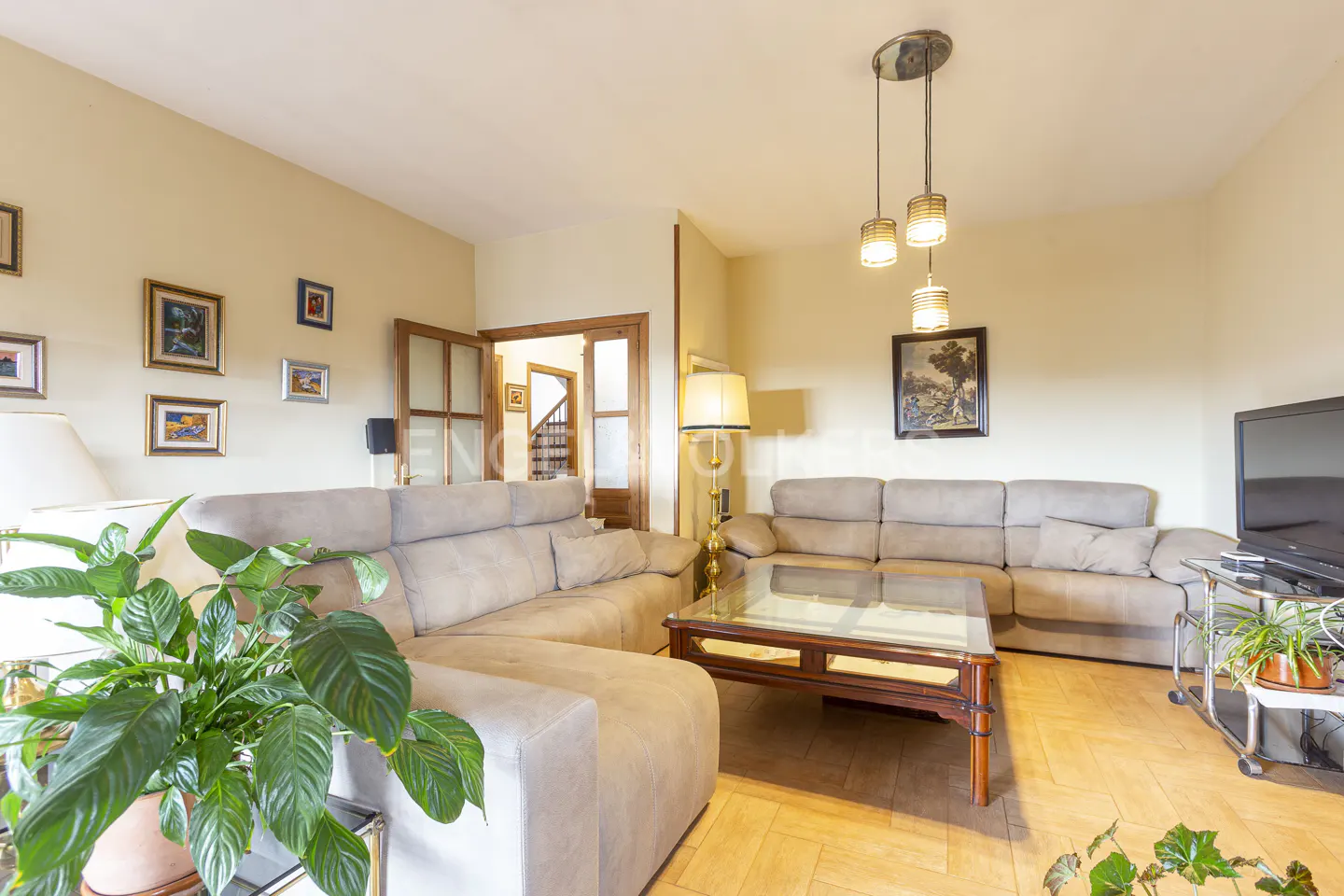 Living room with beige walls, a large sectional sofa, a glass-topped coffee table, and a doorway leading to a staircase.