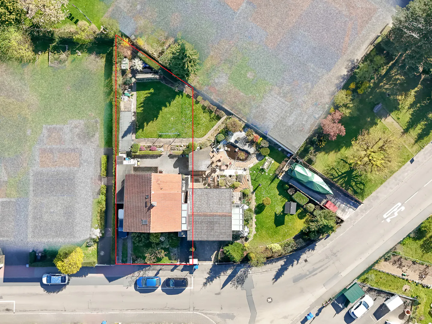 Aerial view of a house with a red tile roof, a green lawn, a pond, and a boat covered with a green tarp.