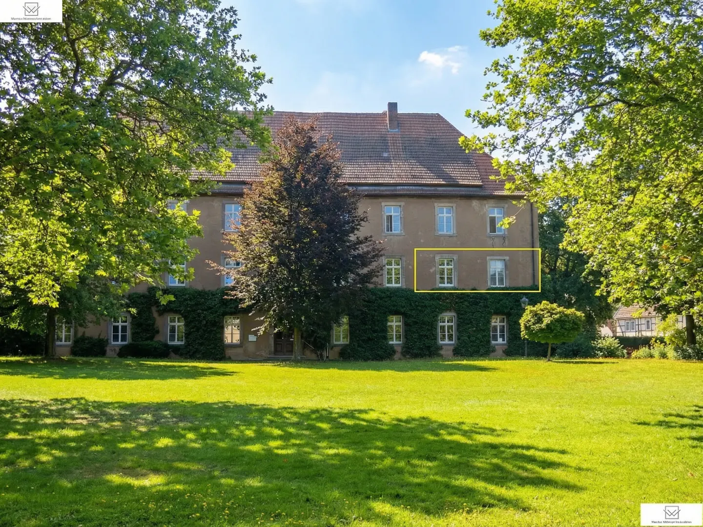 Exterior view of a tan building with a red tile roof, green lawn, trees, and ivy. A yellow box highlights a section of the building.