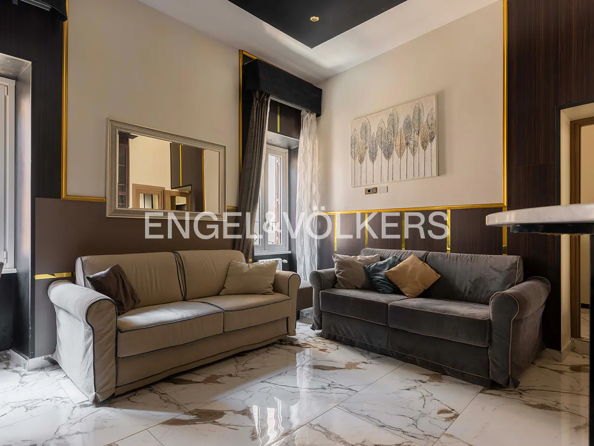 Living room with beige and gray sofas, marble floors, and a window with gray curtains. An abstract painting hangs on the wall.