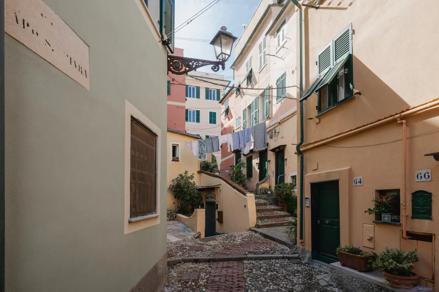 A narrow, cobblestone street in Italy with colorful buildings and laundry hanging overhead.