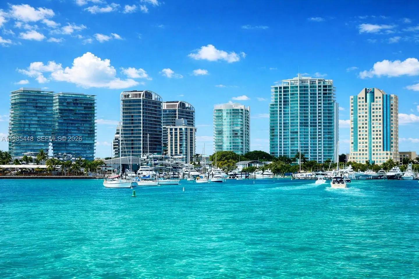 Turquoise water view of Miami skyline with boats docked in front of high-rise buildings under a blue sky with white clouds.
