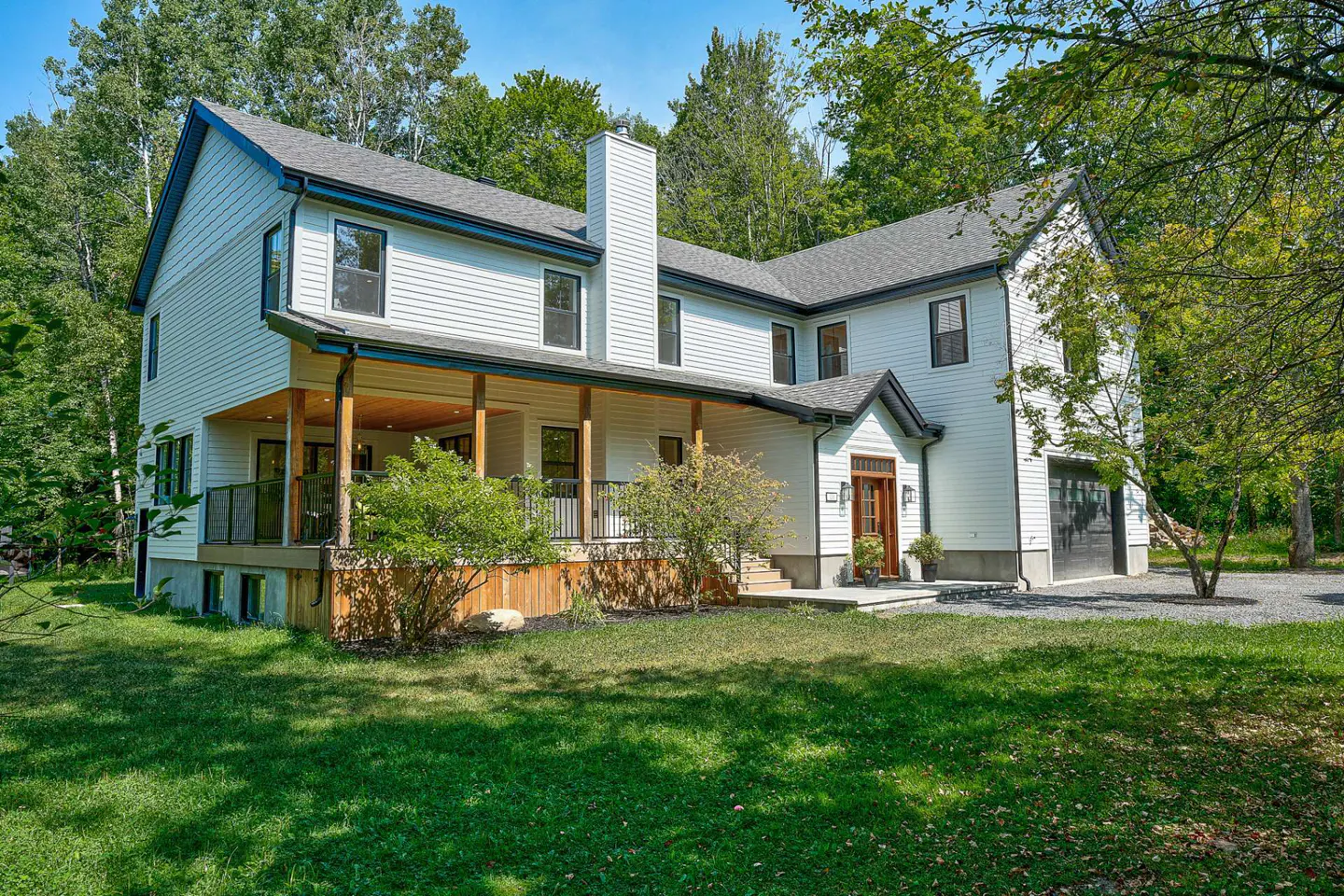 Exterior view of a two-story white house with a gray roof, black trim, and a covered porch surrounded by green trees and grass.