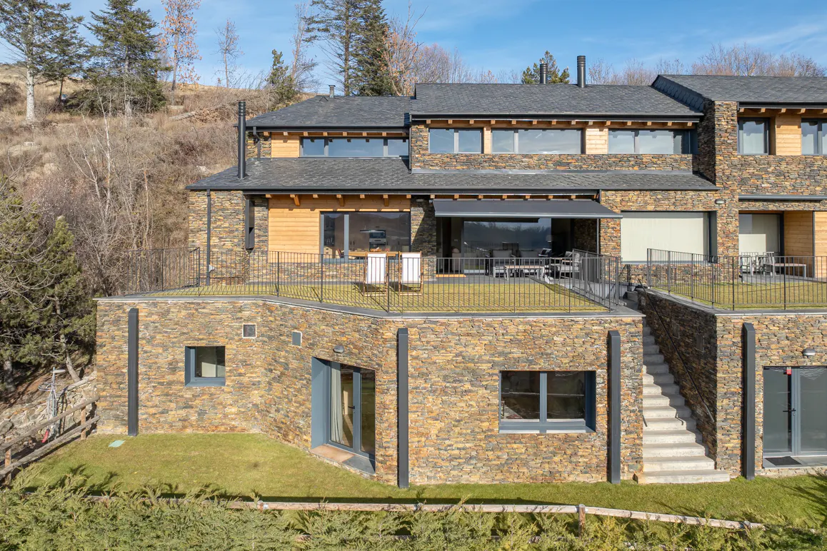 Exterior view of a multi-story stone house with a rooftop patio and a staircase leading to the ground level.