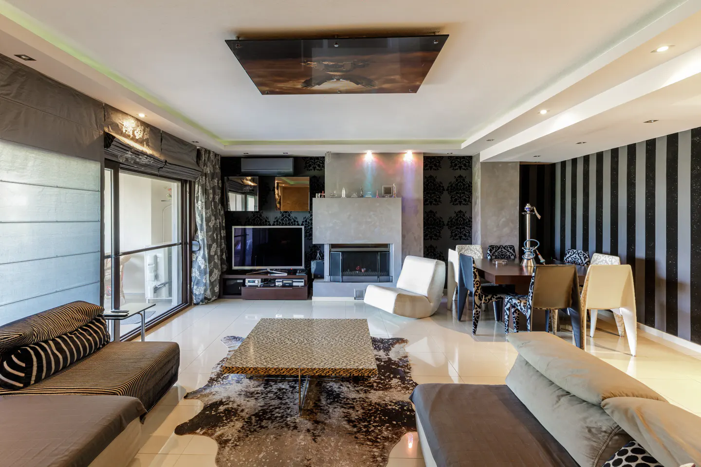 A modern living room with sofas, a dining table, and a fireplace. The walls are decorated with black and white wallpaper.