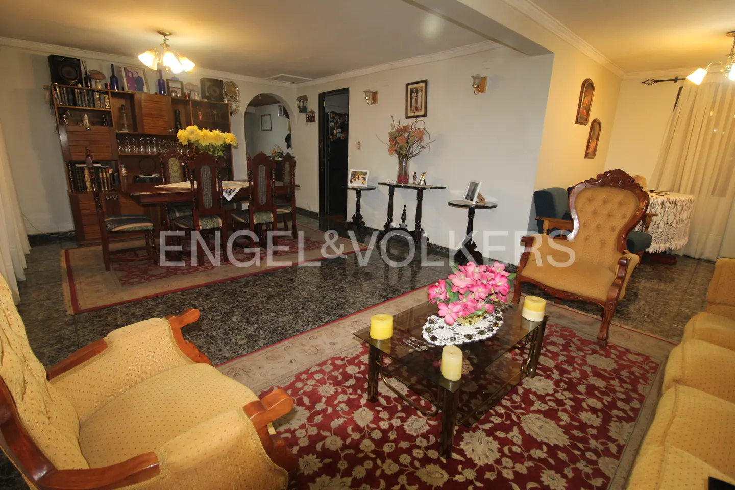 Living room with yellow armchairs, a glass coffee table with pink flowers, and a dining area with a wooden hutch.