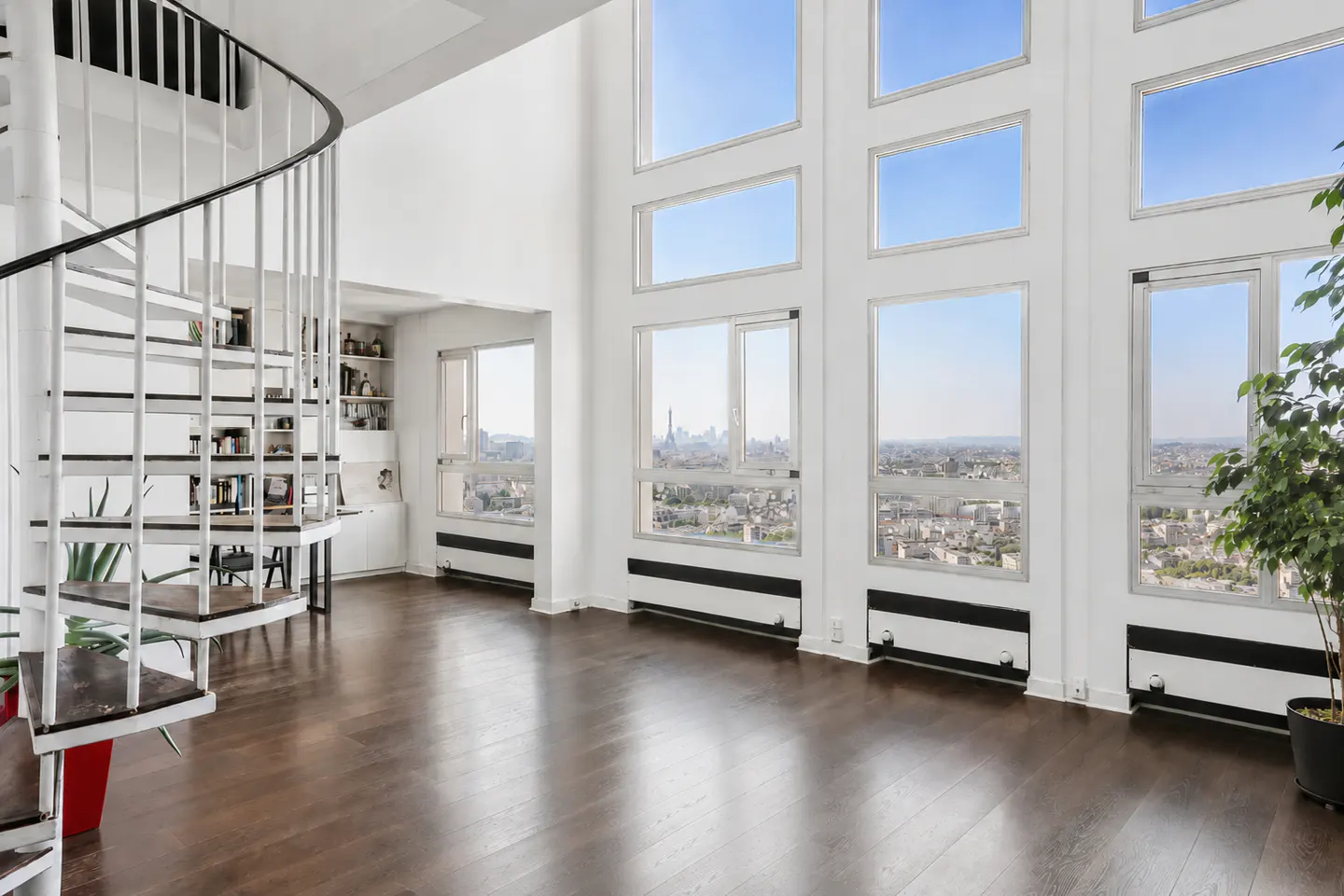 Bright, modern apartment interior with a white spiral staircase, dark wood floors, and a wall of windows overlooking a city skyline.