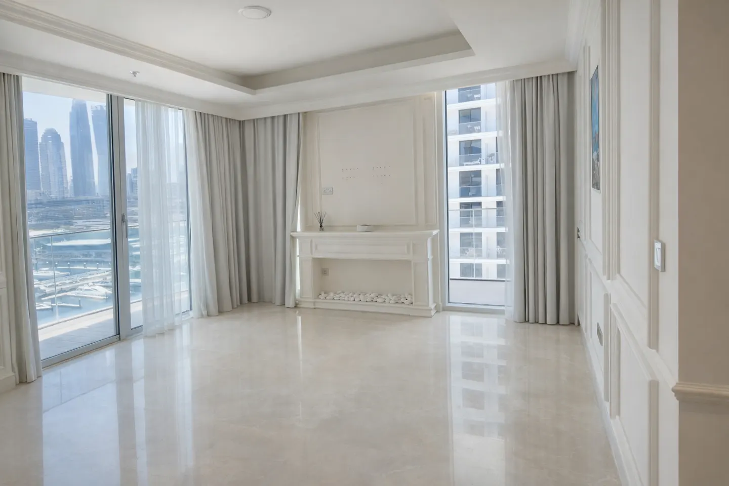 Bright, empty room with marble floors, white walls, and large windows. A decorative fireplace sits against the wall, and sheer curtains hang by the windows.