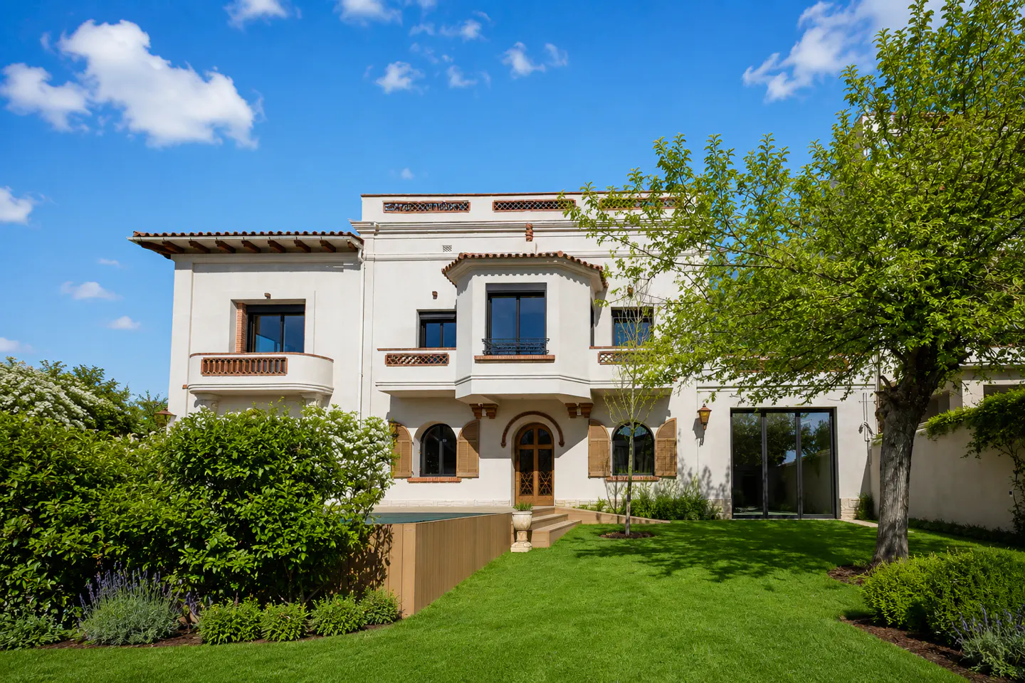 A two-story white house with a red tile roof, a green lawn, and a blue sky.