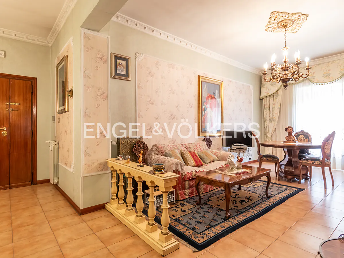 Living room with floral wallpaper, chandelier, sofa, coffee table, and dining table with chairs. Brown tile floor.